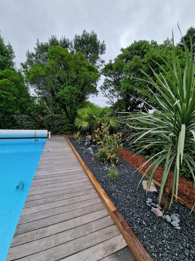 Terrasse bois au bord de la piscine avec massif exotique en traverses