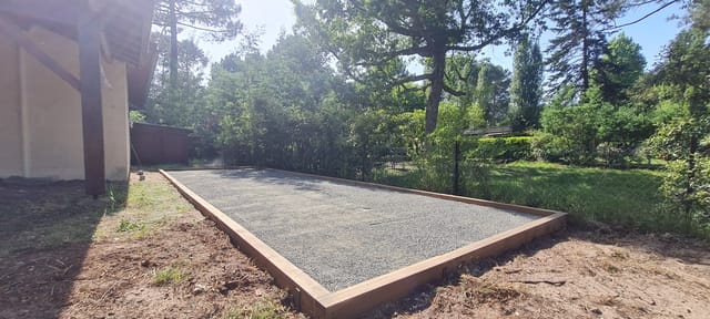 Terrain de pétanque encadré de traverses bois dans un jardin arboré