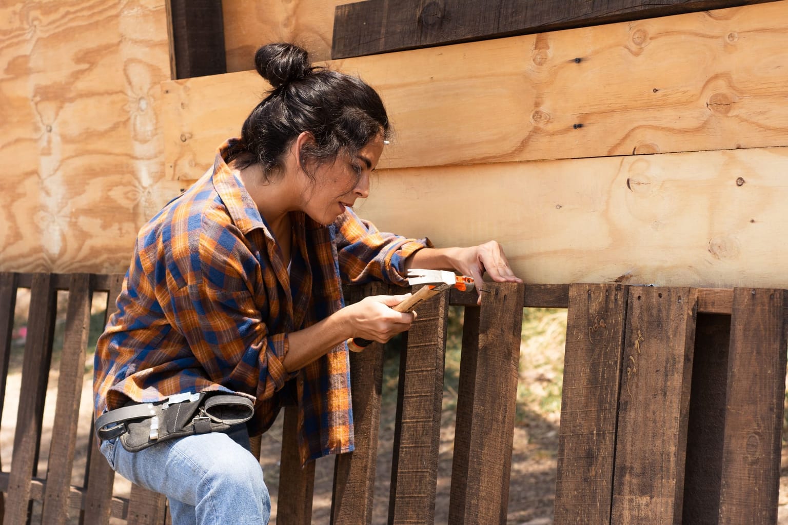 Femme clouant une latte sur une clôture en bois, marteau à la main