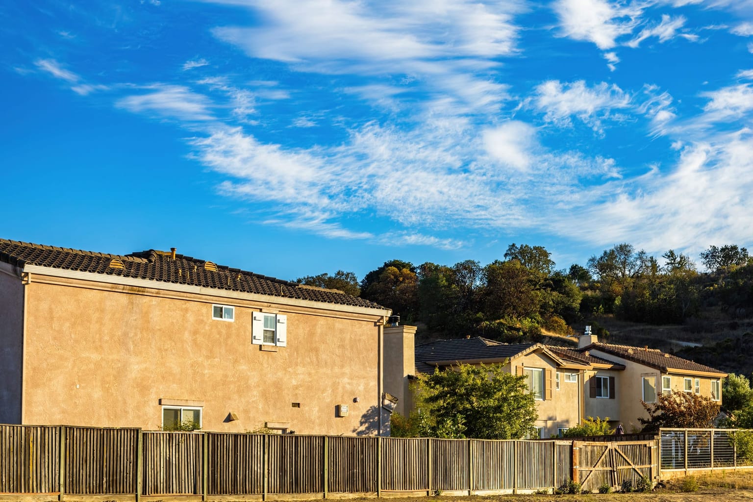 Clôture en bois délimitant des maisons de lotissement sous un ciel bleu
