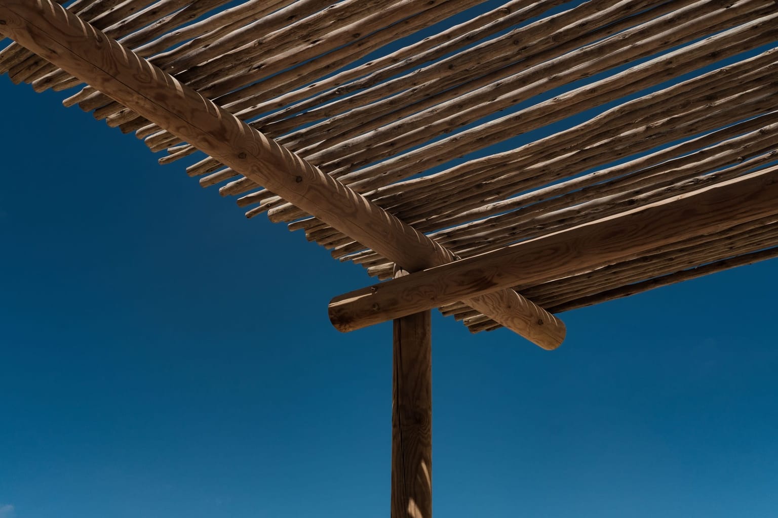 Charpente en bois d'une pergola se détachant sur un ciel bleu